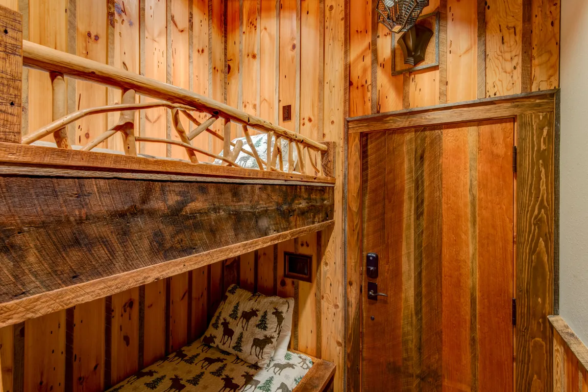 This image shows a single bunk bed against wooden paneling, with a charming decorative wall mount. The compactness and warmth of the space, along with its rustic character, suggest a secluded corner designed for comfort and quiet moments.