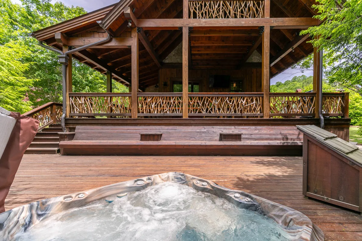 A spacious wooden deck with a hot tub overlooks natural greenery and the exterior of the house. The deck provides ample space for outdoor entertaining, relaxing in the hot tub, and enjoying the tranquil setting. The setup suggests opportunities for barbecues, gatherings, and unwinding in nature.