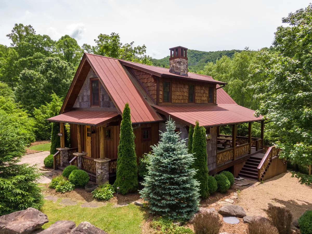 The hero image showcases a charming wooden cabin with a spacious porch, a striking stone chimney, and beautifully landscaped gardens, all set against the tranquil mountain backdrop of Banner Elk. The porch captures the warm glow of sunset, inviting guests to relax and savor the peaceful natural surroundings.