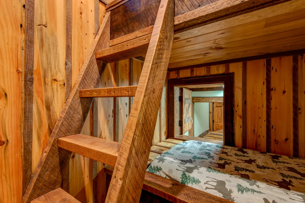 The image features a wooden bunk bed with a decorative ladder, wooden walls, and patterned bedding. The doorway hints at a crawl space entrance, and the intimate scale of the room suggests a tucked-away spot just for kids. The warm tones and textures reinforce the sense of a welcoming, secret retreat.