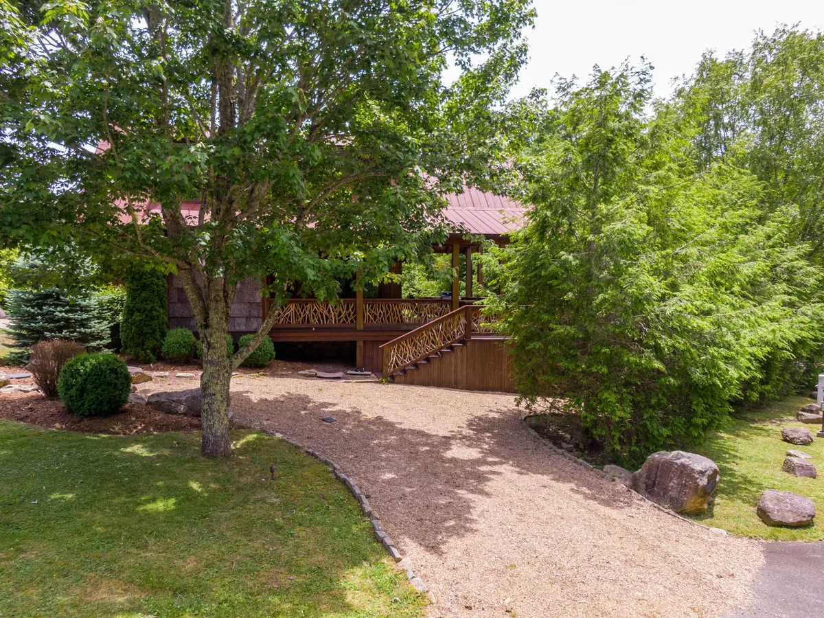 This exterior image features a welcoming wooden porch surrounded by lush green foliage and a gravel pathway, with stone accents enhancing the rustic charm. The porch, set against a tranquil backdrop, invites guests to relax and enjoy the natural mountain environment, reflecting the eco-conscious and comfortable vibe described in the section.
