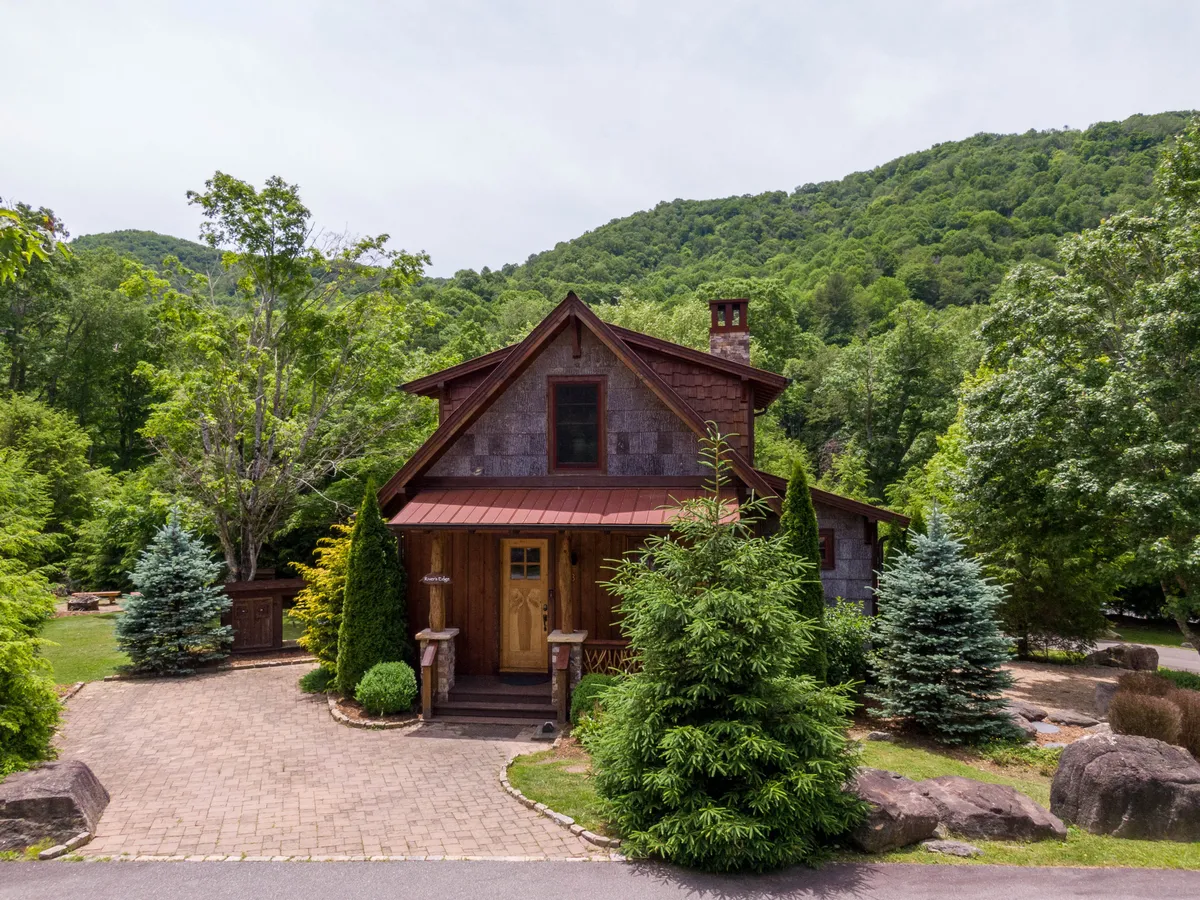 A welcoming view of the cabin’s front door framed by lush greenery, with a unique roof design and a peaceful porch inviting relaxation. The setting hints at outdoor comfort and seamless access to nature.