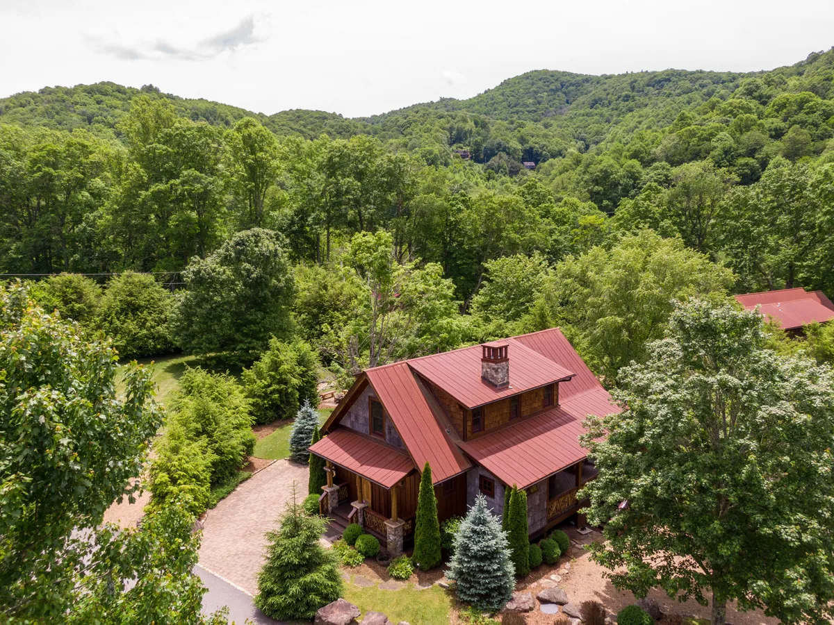 A rustic house with a red metal roof sits amid vibrant greenery, with a stone pathway leading into an expansive outdoor area. The setting is tranquil and suggests immediate proximity to trails and outdoor activities.