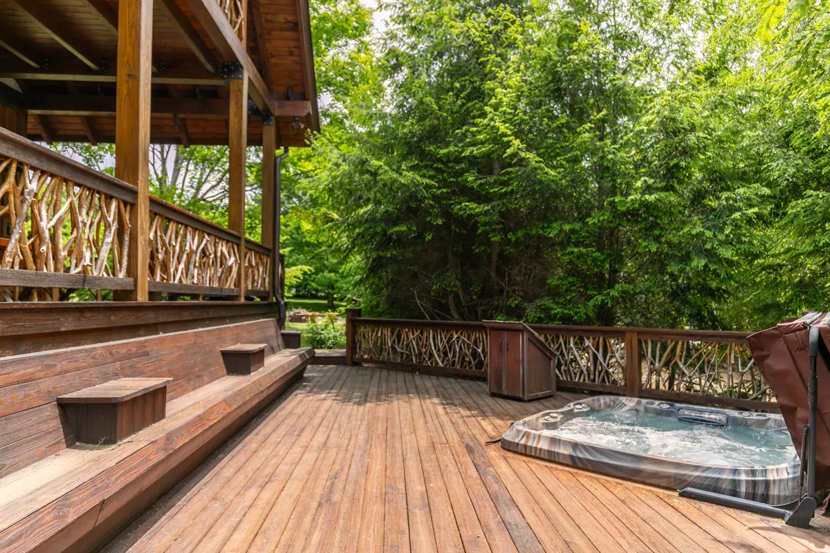 A wooden deck features a hot tub with inviting seating and is enveloped by natural greenery. The outdoor space radiates tranquility and offers an ideal spot for both morning and evening relaxation after exploring the river.