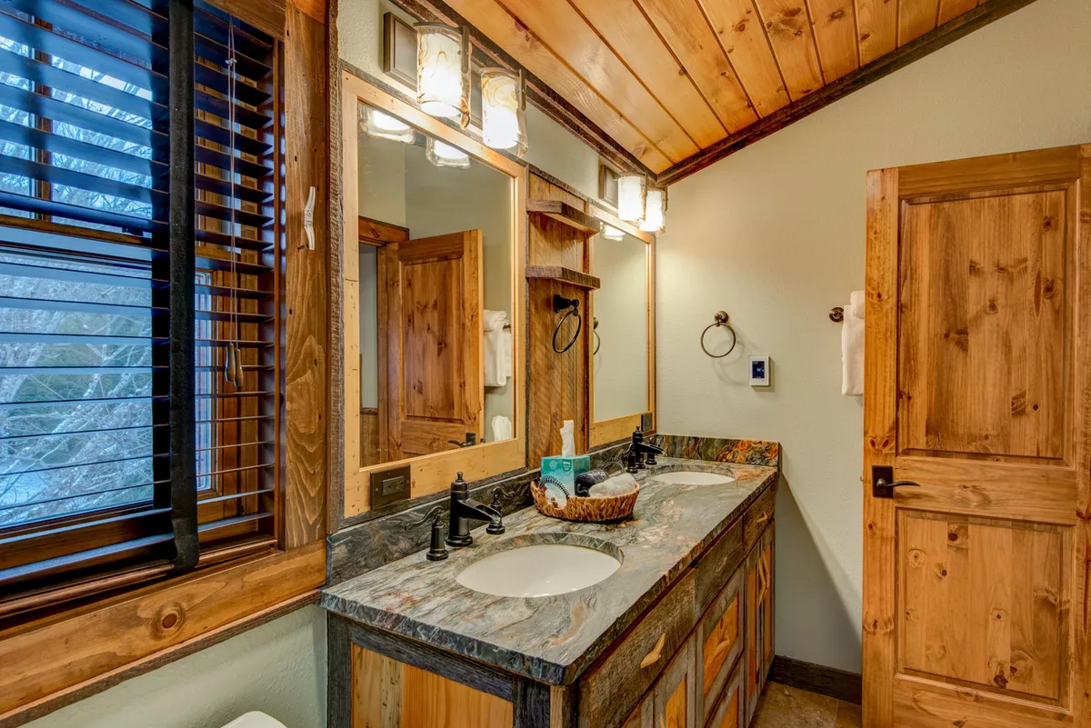 A stylish bathroom interior with a double sink vanity, large mirror, wooden cabinetry, and elegant lighting fixtures. The space is both practical and indulgent, ideal for relaxation and self-care routines.
