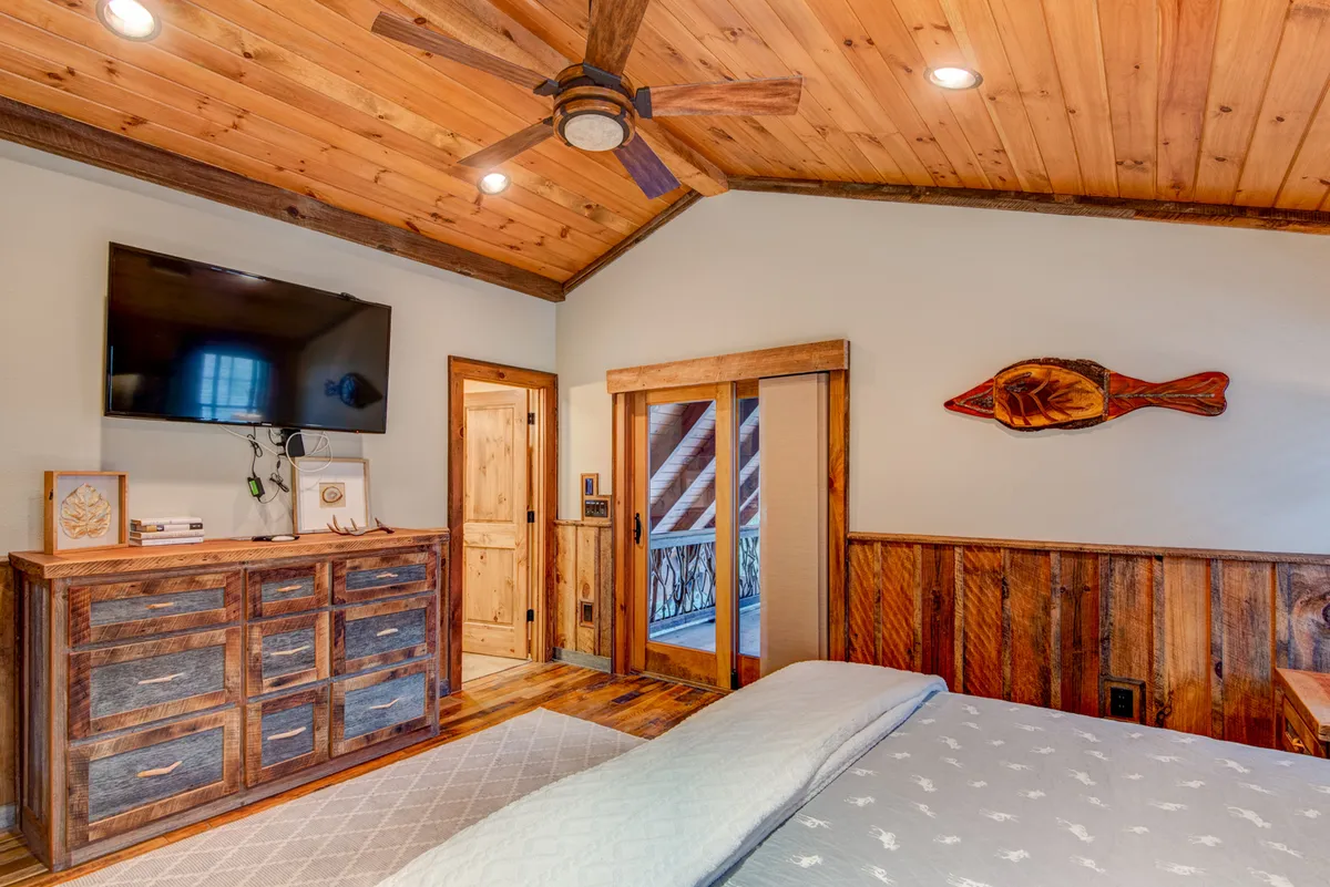 A peaceful bedroom scene featuring a wooden dresser, a wall-mounted TV, sliding doors that likely open to an outdoor view, and rustic decorative touches. The bed is positioned to take in the sunrise, and the space feels both private and comfortable.